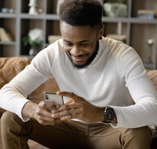 A man sitting on a sofa looking at his phone smiling